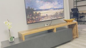 Ein modernes Wohnzimmer mit einem an der Wand befestigten Flachbildfernseher, einer hölzernen Sitzbank mit einer Schale und einem kleinen Blumentopf.