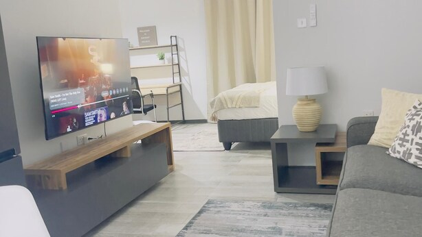 Ein modernes Wohnzimmer mit Flachbildfernseher, einer Couch, einem Couchtisch und einem Bett im Hintergrund.