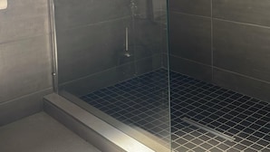 Eine moderne Dusche mit Glastür, dunklen Fliesenwänden und einem Metall-Brausekopf.