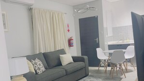 Ein modernes Wohnzimmer mit einem grauen Sofa, einem Holztisch und einem Essbereich mit weißen Stühlen.