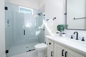 A modern bathroom with a glass-enclosed shower, a white toilet, and a vanity with a mirror and sink. - Waterfront, Gameday Ready, Kayak, Dock, EV Charger - 4 Bed/3 Bath (Dadeville)