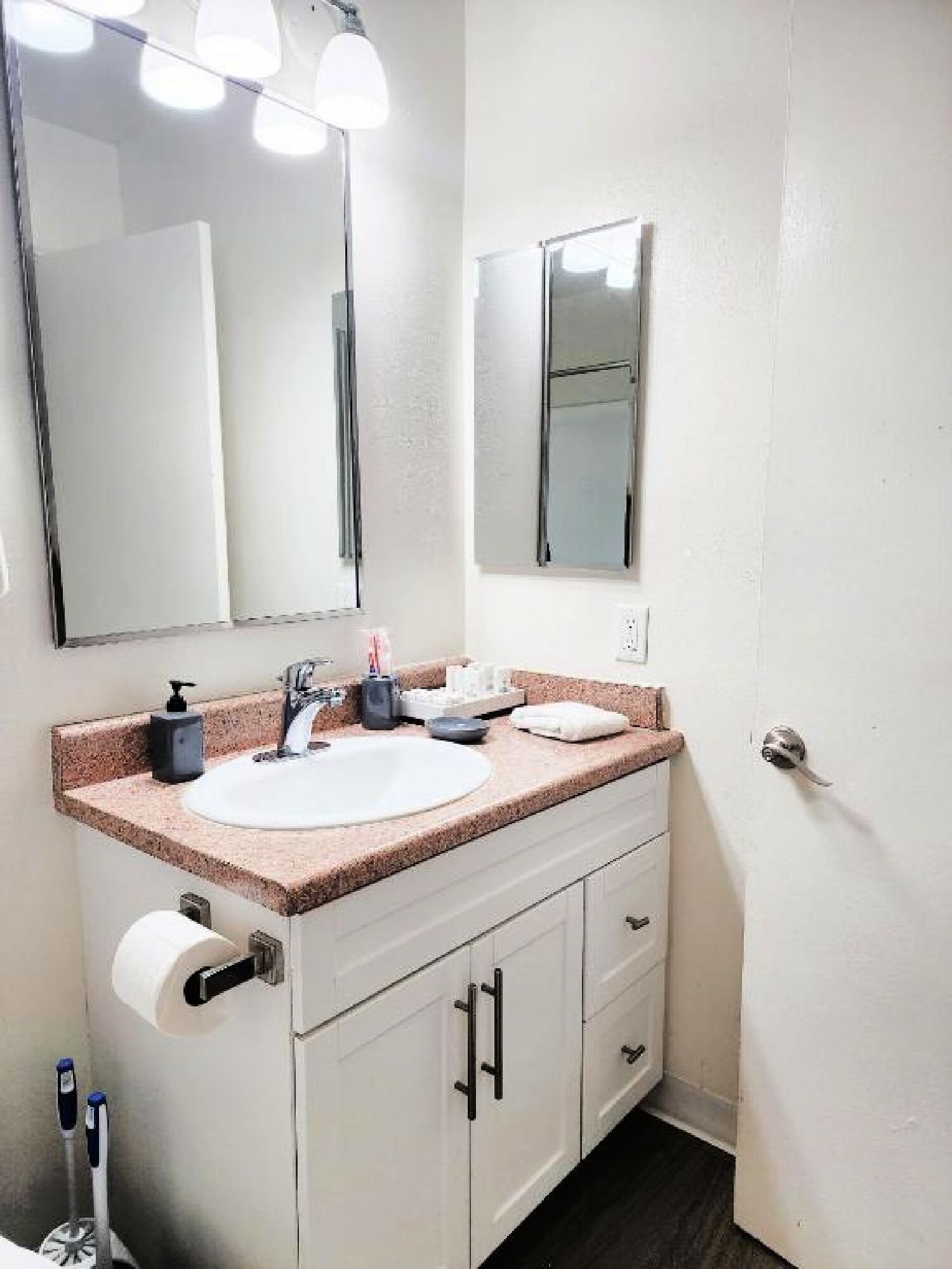 Un baño con lavamanos blanco, un espejo y un inodoro. Hay artículos de aseo en la encimera del lavamanos.