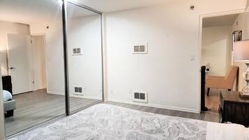 Une chambre avec un grand miroir, un lit recouvert d’une couvre-lit à motifs, une chaise et un bureau avec une lampe.