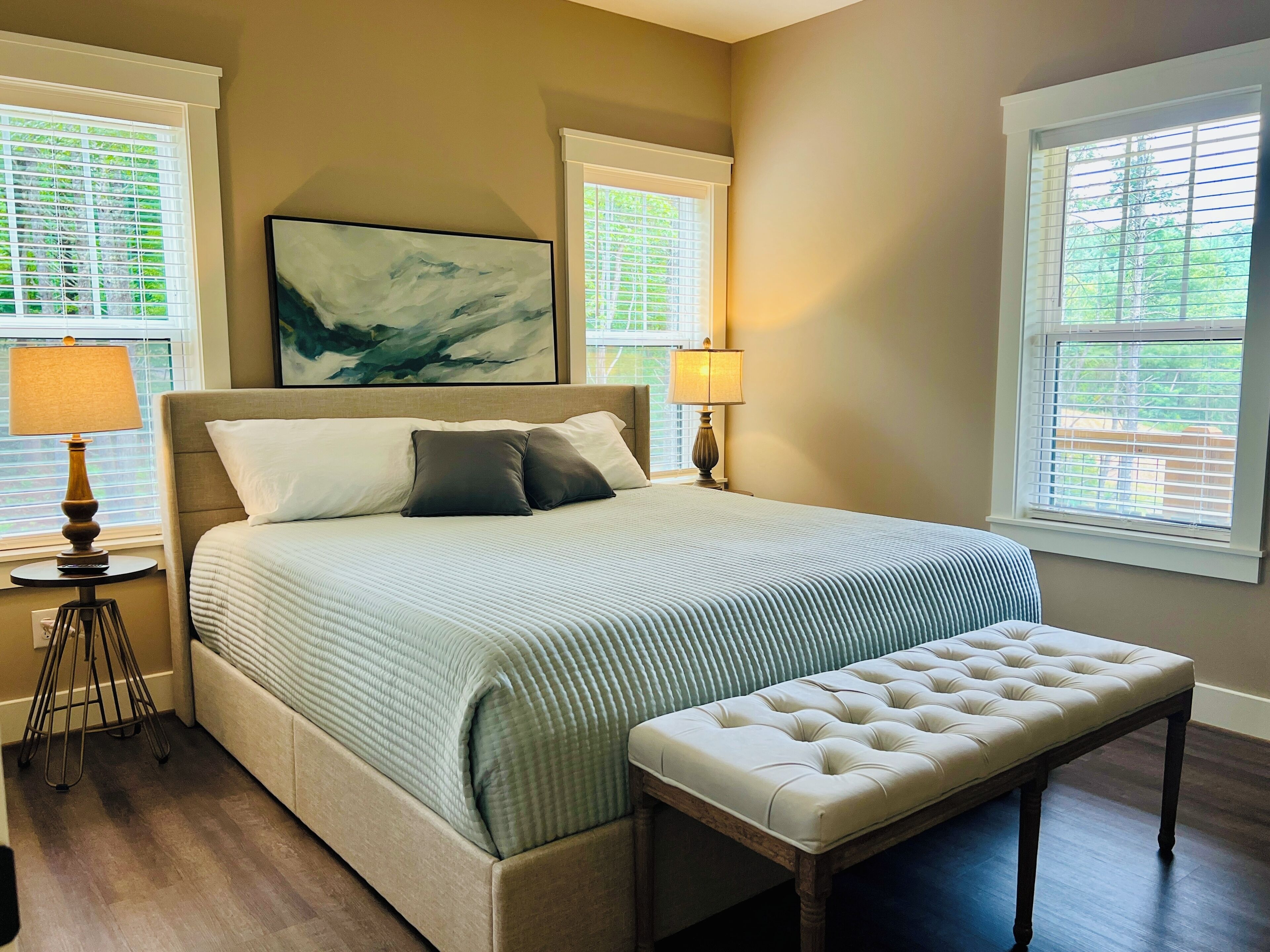 A bedroom with a bed, a bedside table with a lamp, a bench, and a painting on the wall.
