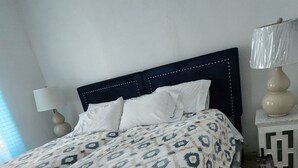 Una cama bien hecha con una colcha estampada, una lámpara de noche y una mesita con lámpara.