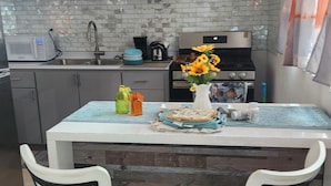 Una cocina con encimera blanca, dos sillas blancas con estructura negra, un lavamanos y una estufa.