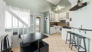 A modern kitchen with white cabinets, a dark countertop, and a built-in oven. There is a dining area with a table and chairs, and a staircase with a railing. - Seascape loft with stunning Gulf Views! (Panama City Beach)