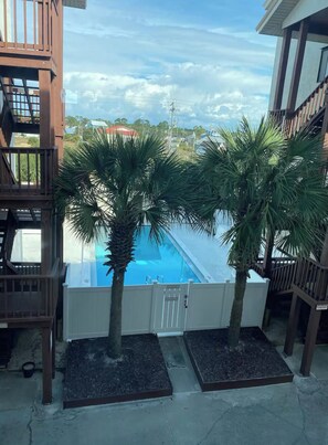 A pool area with two palm trees and a white fence. - Seascape loft with stunning Gulf Views! (Panama City Beach)