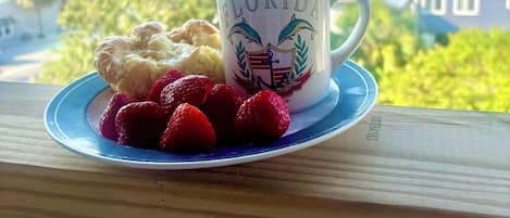 A mug with "FLORIDA" and dolphins on a plate with strawberries and a pastry, overlooking a coastal view.