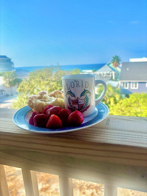 A mug with "FLORIDA" and dolphins on a plate with strawberries and a pastry, overlooking a coastal view.