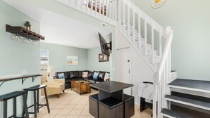 A spacious living area with a kitchen counter, bar stools, a sofa, and a staircase. - Seascape loft with stunning Gulf Views! (Panama City Beach)