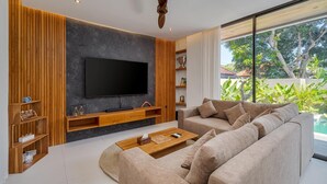 Una sala de estar moderna con un televisor de pantalla plana grande, paneles de madera, un sofá color beige y vista a una piscina.