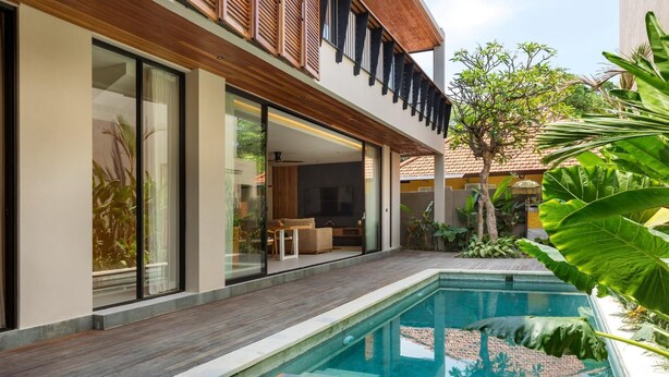 Una casa moderna con piscina, terraza de madera y plantas tropicales.