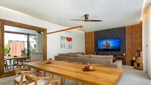 Una sala de estar moderna con una mesa de comedor de madera, sillas, un sofá y una televisión.