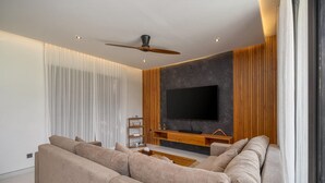 A modern living room with a large flat-screen TV, a ceiling fan, and a large beige sectional sofa. - Villa Sunshine – Sparkling Style & Spacious Comfort in Sanur (Sanur)