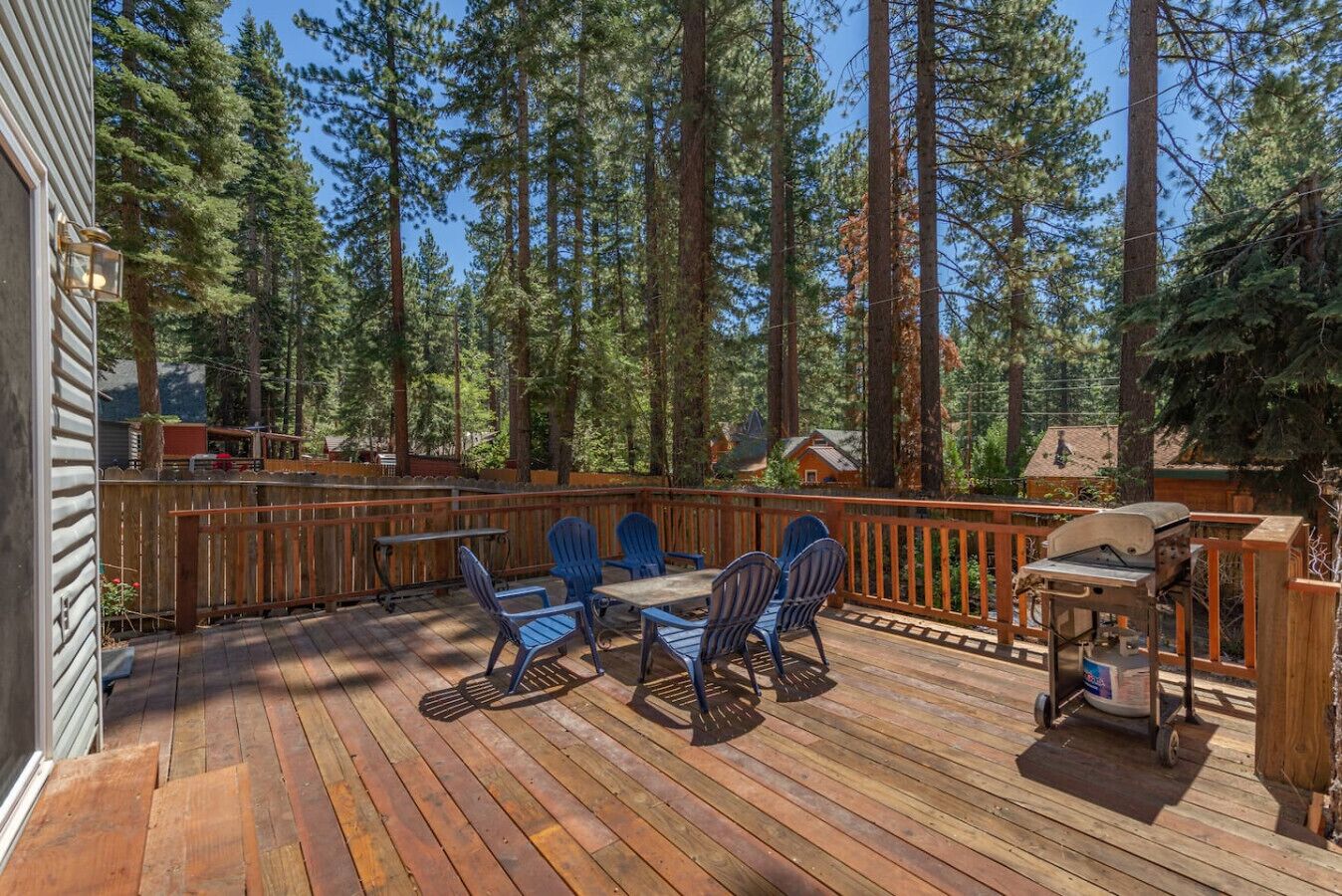 A wooden deck with a table and chairs, surrounded by tall trees.