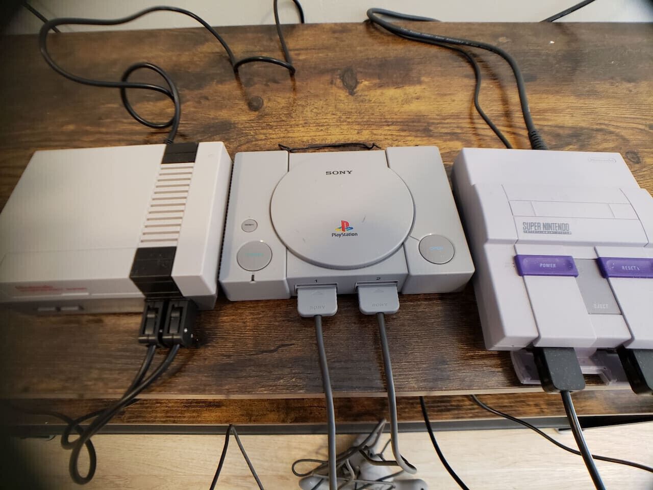 Una consola PlayStation conectada a una consola Super Nintendo sobre una mesa de madera.