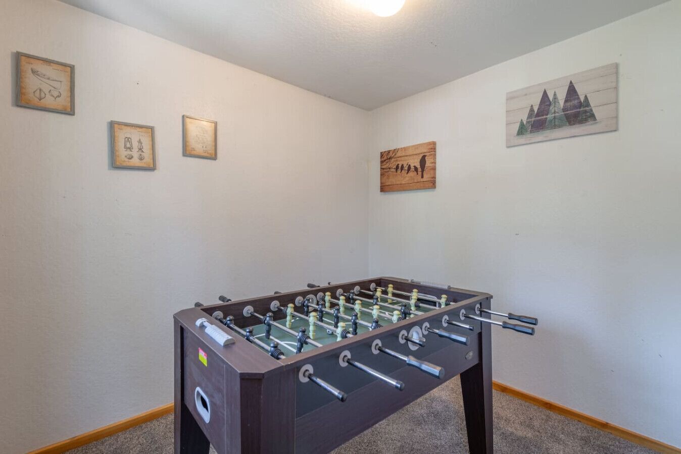 Une pièce avec une table de baby-foot, des tableaux encadrés aux murs et un luminaire au plafond.