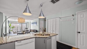 Una cucina con piano di lavoro in granito, lavello in acciaio inossidabile e pensili grigi. Sopra il lavello ci sono luci a sospensione e un tappetino d'ingresso nero.