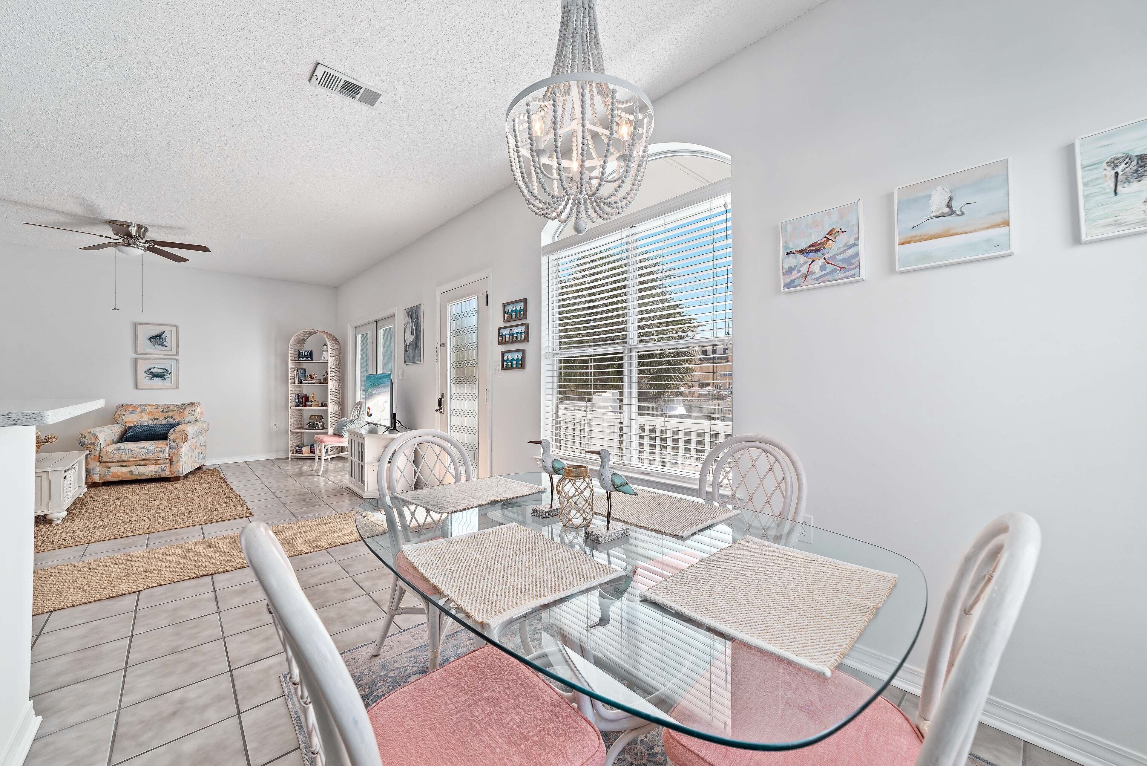 A dining area with a glass table, white chairs, and a chandelier.