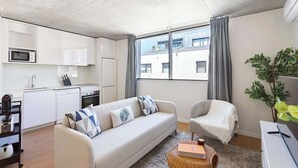 A modern living room with a sofa, a chair, a small table, and a kitchen area with white cabinets and appliances. - Modern Family Flats w/ Terrace by HostWise (Porto)