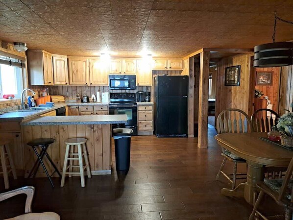 A rustic kitchen with wooden cabinets, a microwave, a refrigerator, and a dining area with a table and chairs.