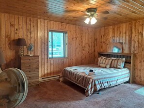 A wooden-paneled room with a bed, dresser, and a ceiling fan.