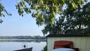 Un espace extérieur verdoyant avec deux chaises bleues, un bateau et une table abritée, le tout situé près d’un lac.