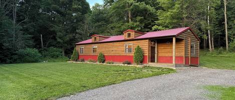 A wooden cabin with a red roof, surrounded by a well-maintained lawn and trees.