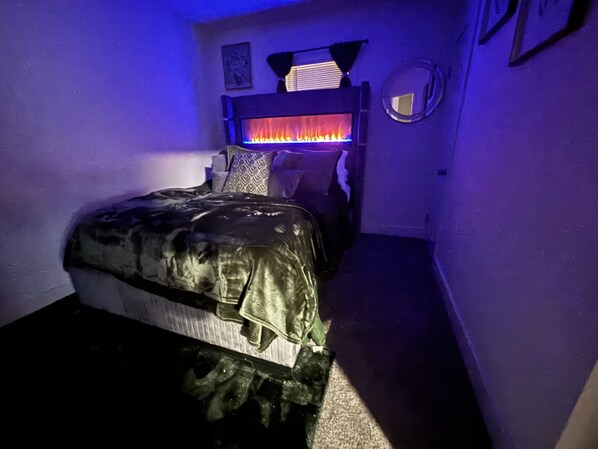 Un dormitorio con cama, un calefactor de pared y un espejo redondo pequeño.