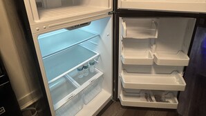 Avoin jääkaappi, jossa on useita hyllyjä ja laatikoita, sen yläpuolella oleva puinen kaappi ja puinen lattia.