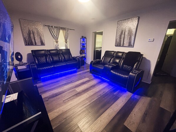 Un salón moderno con un sofá de cuero negro, luces LED azules y un televisor de pantalla plana.