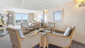 A hotel room with a living area featuring two sofas, a coffee table, and a large window offering a view. - Direct Oceanfront 2/2 | Private Balcony Overlooking the Pool | Garage Parking (Ormond Beach)