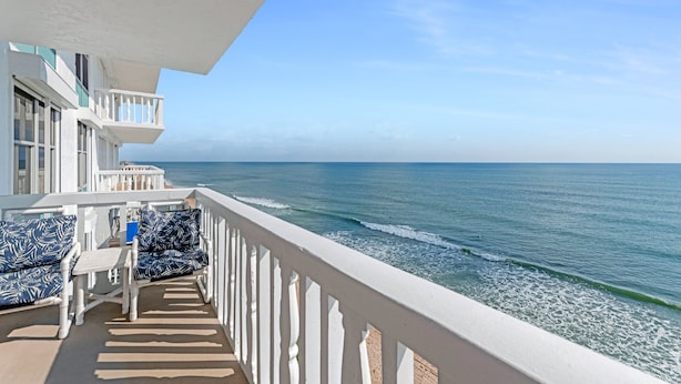 A balcony with a view of the ocean, white railings, and blue patterned outdoor furniture. - Direct Oceanfront 2/2 | Private Balcony Overlooking the Pool | Garage Parking (Ormond Beach)