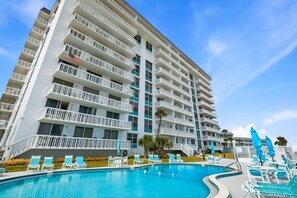 A multi-story hotel with a swimming pool, outdoor seating, and a flag on the building. - Direct Oceanfront 2/2 | Private Balcony Overlooking the Pool | Garage Parking (Ormond Beach)