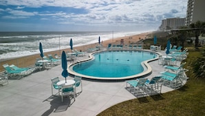 A pool area with lounge chairs and umbrellas, overlooking the beach and ocean. - Direct Oceanfront 2/2 | Private Balcony Overlooking the Pool | Garage Parking (Ormond Beach)