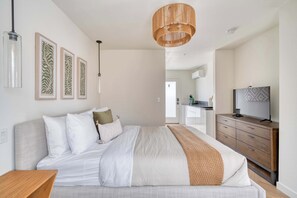 Ein Schlafzimmer mit einem Bett, einer Holzkommode, einem Fernseher und gerahmten Kunstwerken an der Wand.