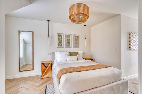 Ein modernes Schlafzimmer mit einem großen Bett, hölzernen Nachttischen, einer Pendelleuchte und gerahmten Kunstwerken an der Wand.