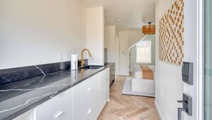 A modern kitchen with a black marble countertop, white cabinets, and a wooden floor. - Alberta Arts-tastic Mother-In-Law Suite (Portland)