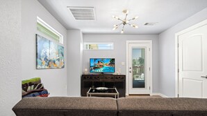 A living room with a grey sofa, a flat-screen TV, a ceiling fan, and artwork on the wall. - Sinatra Cottage · Classic Charm by Ocean Town (Galveston)