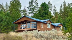 A wooden cabin with a blue roof, large windows, and a balcony with chairs.