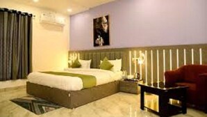 A modern hotel room with a large bed, a nightstand, a red armchair, and a ceiling fan. - Hotel Samdariya Gold - Rewa (Huzur)