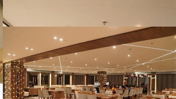 A spacious banquet hall with multiple tables and chairs, a high ceiling with recessed lighting, and a modern architectural design. - Hotel Samdariya Gold - Rewa (Huzur)