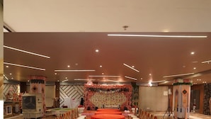 A banquet hall with a stage, round tables, and a decorative backdrop. - Hotel Samdariya Gold - Rewa (Huzur)