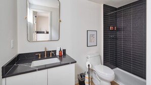 A modern bathroom with a black marble sink, a white toilet, and a black tiled shower area.