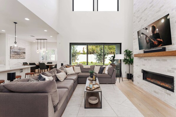 A modern living room with a sectional sofa, a coffee table, a fireplace, and a TV mounted on the wall.