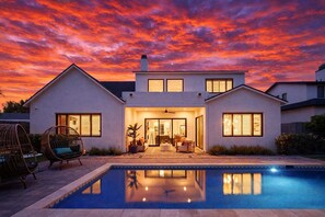 A modern two-story house with a swimming pool, large windows, and a patio area.