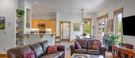 A spacious living room with leather sofas, a wooden coffee table, and a kitchen area in the background.