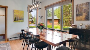 Uma área de refeições com uma grande mesa de madeira, cadeiras pretas e um lustre pendurado.