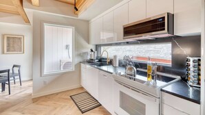 Una cocina moderna con armarios blancos, una estufa de acero inoxidable y una ventana que da a un muro de ladrillo.